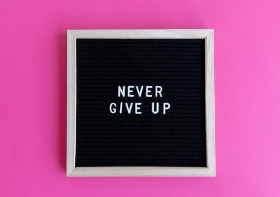 A framed letter board with 'NEVER GIVE UP' on a vibrant pink background.