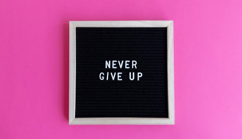 A framed letter board with 'NEVER GIVE UP' on a vibrant pink background.