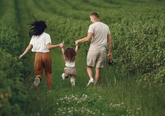 A joyful family strolls through a lush green field, enjoying quality time together.